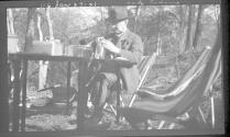 George Eastman looking into jar at picnic table, Oak Lodge Trip