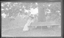 May Gifford on bench under large tree, Oak Lodge Trip