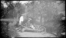 [Man giving woman ride in large wooden wheelbarrow]