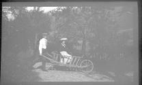 [Man giving woman ride in large wooden wheelbarrow]