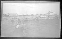 [People swimming in ocean, amusement pier in distance]