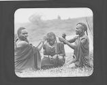 Two native women braiding another woman's hair