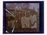 [Group of eight African American children standing in line, sticking out tongues or candy in mouth]