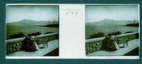 [Woman seated at table overlooking water and mountains]