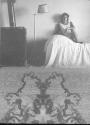 [Woman seated in opening between portrait of man and textured rectangular opening]