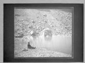 [Figure seated beside a river]