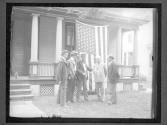 [Group of men, including William Jennings Bryan by porch with American flag on display]