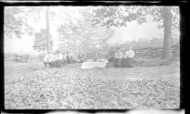 George Eastman and guests sitting by rail fence, Oak Lodge Trip