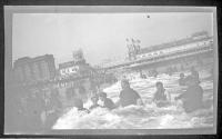 [People swimming in ocean, amusement pier in distance]