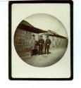 Three Men in Front of Grass-Roofed Buildings