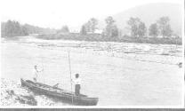 Men in canoe, logs on riverbank in distance, Grand Cascapedia Trip