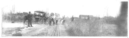 Wagon, houses, men and dogs on dirt road, Oak Lodge Trip