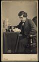 [Prof. Dunn, reading book and posed with stoppered bottles and beaker]