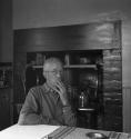 [Charles Sheeler smoking by a table]