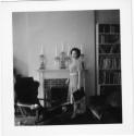 [Woman standing before fireplace]