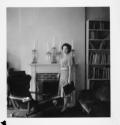 [Woman standing before fireplace]