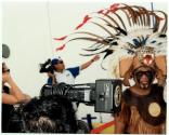 [Cruise photographer with camera equipped with a Metz flash unit photographing a subject in feathered headdress, face makeup and native garb]