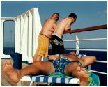 [Man sprawled on deck chair, two other men at railing of cruise ship]