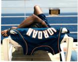 [Man in deck chair draped with basketball singlet (view from behind)]