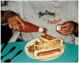 [Close up of woman pouring ketchup on hot dogs on plate of food]