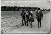 [Group of four young adults carring books on road, dog running alongside]