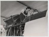 [Woman worker straddling fuselage of uncompleted aircraft]