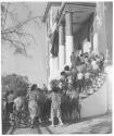 [Children, with two older girls, ascending steps into building]