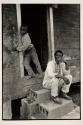 [Man sitting on cinder block steps, boy in doorway]