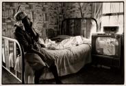 [Woman sitting on bed watching television]