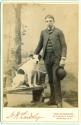 [Studio portrait of standing young man, white dog with black markings sitting on bench]