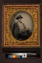 [Seated man wearing cape and hat, holding a cat]