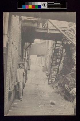 [Two men in alley with one hat on ground]