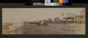 [Man and woman sitting in boat on beach with other boats along shore line]
