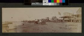 [Man and woman sitting in boat on beach with other boats along shore line]