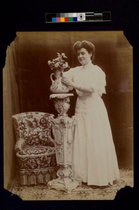 [Women standing by flowers in vase on pedestal]