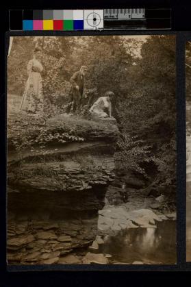 [Two women with older man looking over the side of a small cliff]