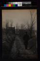 [Man wearing hat walking down dirt road]