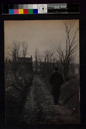 [Man wearing hat walking down dirt road]