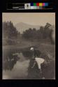[Two men bending over pond]