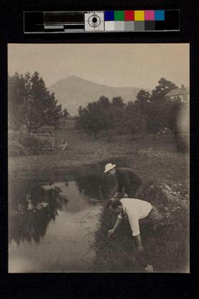 [Two men bending over pond]