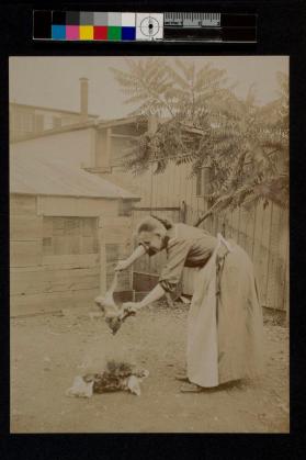 [Woman standing over fire holding chicken]