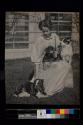 [Woman sitting in grass holding three dogs]