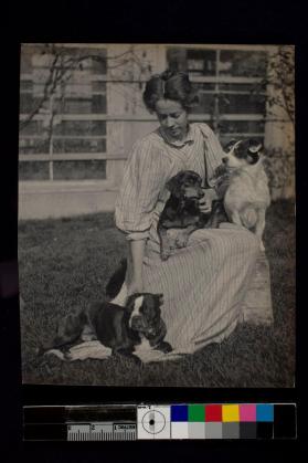 [Woman sitting in grass holding three dogs]