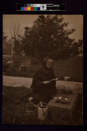 [Woman kneeling in cemetery reading book]
