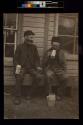 [Two men sitting on porch drinking from mugs]