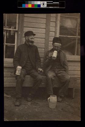 [Two men sitting on porch drinking from mugs]