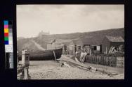 [Two men by fishing sheds and boat]