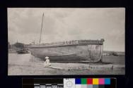 [Woman sitting by large boat, "LT104"]