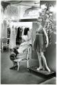 [Woman sitting in clothing store near mannequin]