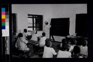 [Teacher at blackboard in classroom]